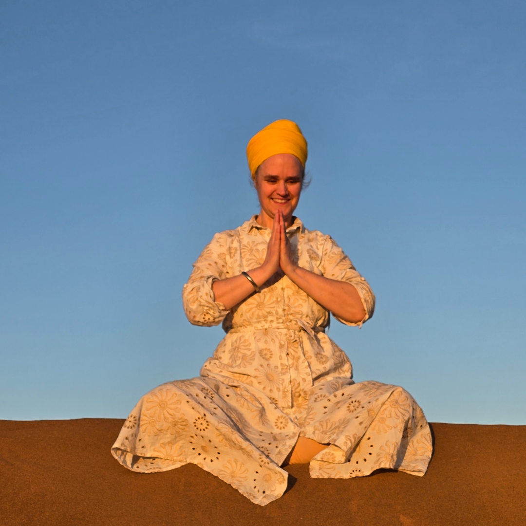 A peaceful yogi sits cross-legged at sunrise, hands in prayer pose, surrounded by soft green nature—symbolizing heart-centered awareness and balance.