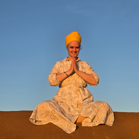 A peaceful yogi sits cross-legged at sunrise, hands in prayer pose, surrounded by soft green nature—symbolizing heart-centered awareness and balance.